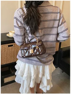 Detailed close-up shot of a stylish dark brown quilted chain shoulder bag worn by woman.