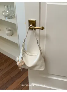Detail view of stylish white slouchy shoulder dumpling bag hanging on wooden door, daily casual aesthetic.