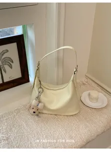 Detailed view of fashionable pale yellow shoulder dumpling bag with cute charm pendant.