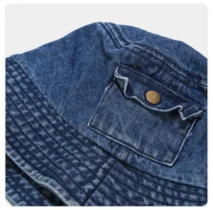 Washed denim bucket hat detail showing textured fabric, practical pocket and metal snap button.