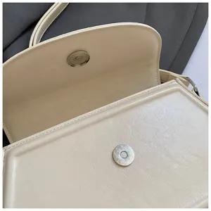 Détail de sac bandoulière beige montrant une fermeture aimantée et cuir souple.