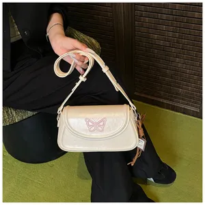 Détail du sac porté épaule beige avec broderie papillon rose et bandoulière réglable.