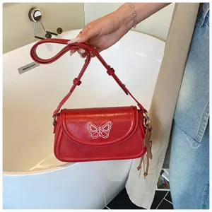 Détail du sac épaule en cuir rouge, broderie de papillon blanc et sangle réglable élégante.