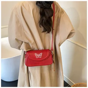 Vue détaillée d'un sac à épaule rouge en cuir avec papillon brodé blanc sur le rabat.