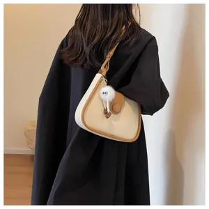 Detail view of a trendy beige crossbody bag with brown trim and cute fluffy charm.