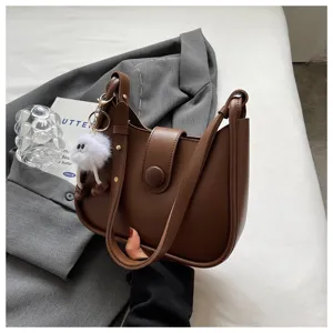 Brown leather shoulder bag featuring simple design, wide strap and cute furry pendant detail.