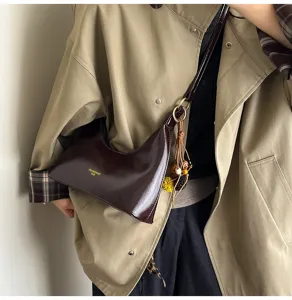 Glossy patent leather underarm shoulder bag with chic metal ring charm and stylish crescent shape.