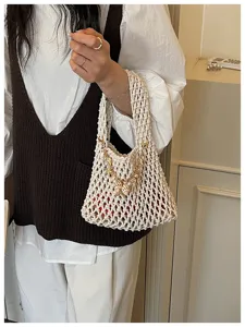 Detailopname van een stijlvolle witte geweven emmertas met delicate schelpbedels en ketting.
