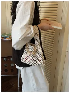 Detailopname van de beige macramé geweven handtas met een delicate schelp- en parelhangerhanger.