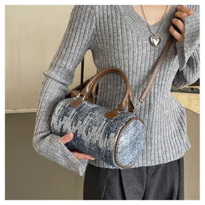 Close-up of stylish barrel handbag with denim texture and brown leather trim for trendy outfits.