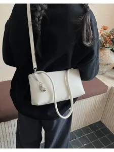 Detail view of stylish white baguette shoulder bag, minimalist casual design with metal pendant.