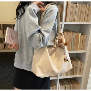 Vue détaillée d'un sac cabas beige décontracté porté par un mannequin près d'une bibliothèque.