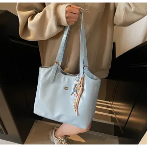 Detail shot of the light blue patent leather tote bag with charming bead pendant and slim straps.
