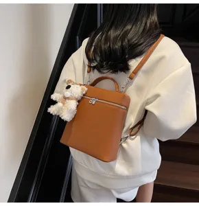 Chic brown leather backpack with cute white bear pendant, stylish daily travel bag for women.