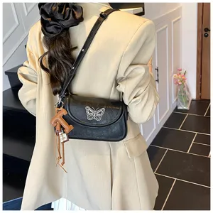 Vue détaillée du sac porté épaule en cuir noir avec papillon argenté et pendentif.