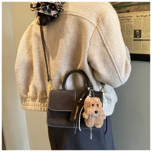 Detail view of dark frosted crossbody bag with white stitching and cute plush puppy keychain.