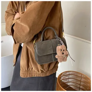 Close-up detail of vintage matte leather crossbody handbag with cute fluffy bear charm.