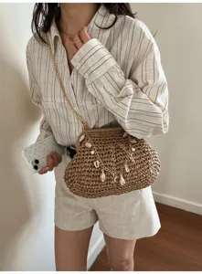 Detail shot of a trendy straw woven crossbody bag with chain and shell pendants worn by model.