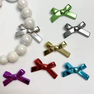 Detail view of glossy metallic bow charms and shiny pearl beads for DIY handmade jewelry.