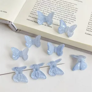 Close-up detail of light blue acrylic butterfly beads with glitter facet design, back hole for DIY hair accessories.