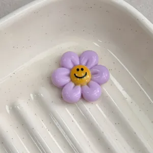 Close up of purple resin flower cabochon with cute smile face, ideal for DIY jewelry making.