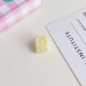 Dettaglio di perla con alfabeto quadrato in acrilico giallo per accessori gioielli.