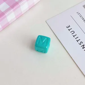 Vista di dettaglio di una perla a cubo in acrilico turchese con lettera M per accessori