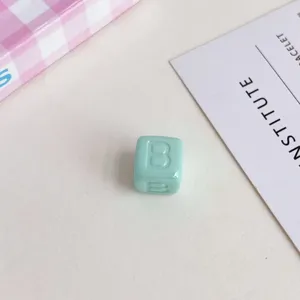 Dettaglio primo piano perlina quadrata con lettera in acrilico, accessorio gioiello DIY.