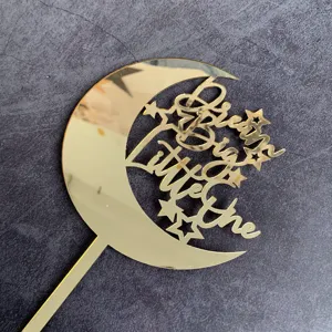Close-up view of a gold acrylic cake topper featuring a crescent moon and star design.