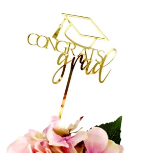 Gold acrylic graduation cake topper detail shot with floral base, elegant party decoration.