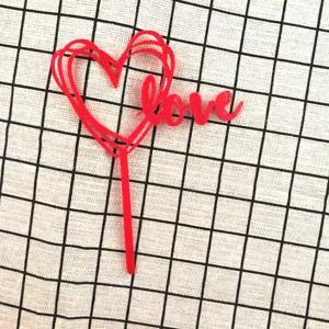 Close-up detail of red acrylic heart cake topper with love lettering for party decoration.