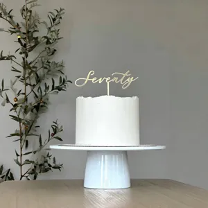 Detail shot of golden acrylic seventy cake topper on frosted white cake for anniversary.