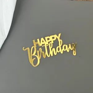 Nahaufnahme von goldenem Acryl Happy Birthday Kuchendekor mit glänzender Metalloberfläche.