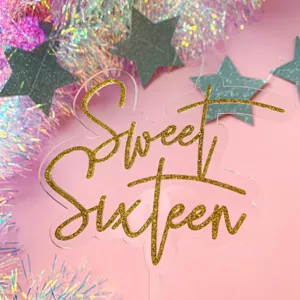 Close-up view of gold glitter Sweet Sixteen acrylic cake topper for sweet birthday party decor.