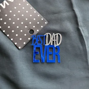 Detailed close-up of blue and silver acrylic Best Dad Ever cake topper on dark textured fabric.