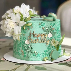 Detalle en primer plano de tarta de cumpleaños verde menta con topper acrílico y decoración.
