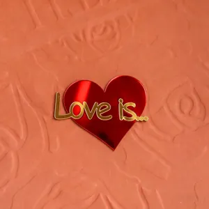 Roter Acryl Herz Tortenaufsatz mit goldener Love is Text Detailaufnahme zum Valentinstag.