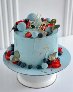 Gros plan d'un gâteau d'anniversaire bleu avec topper en acrylique et fruits frais.