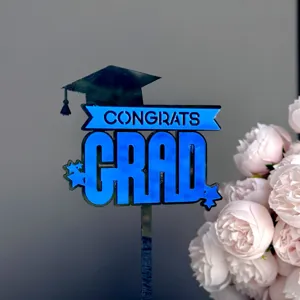 Close-up of blue acrylic graduation cake topper with CONGRATS GRAD lettering and cap design.