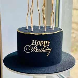 Detailopname van luxe zwart-gouden verjaardagstaart met acrylcake topper en stijlvolle kaarsen.