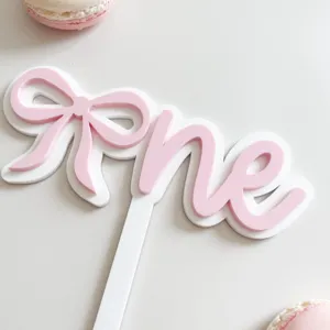 Pink and white acrylic one cake topper with bow for baby birthday party dessert table.