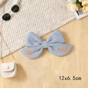 Close-up detail of light blue fabric bow hair clip featuring delicate swan embroidery.
