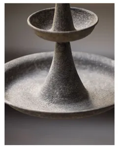 Close-up detail of rustic tiered bird feeder showing rough stone texture and cone pillar.