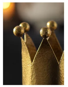 Close-up detail shot of vintage golden crown candle holder, rustic metallic texture surface.