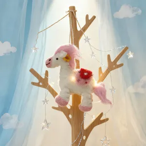 Close-up of cute wool felt pony doll hanging on decorative tree with fairy lights background.