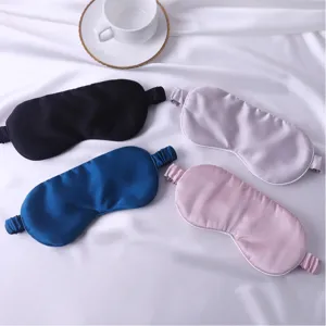 Detail du masque de sommeil en soie quatre couleurs noir bleu gris rose sur fond de tissu blanc.