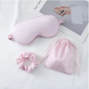 Details des rosa Seiden-Schlafmasken-Sets mit Haargummis und Tasche, glatte Textur Nahaufnahme.