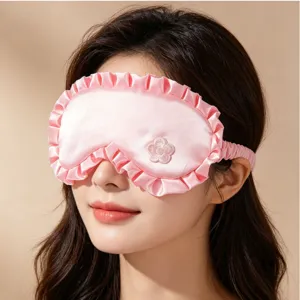 Nahaufnahme einer rosa Satin-Schlafmaske mit Rüschen und zarter Blumenstickerei.