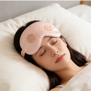 Close-up detail of a soft pink silk sleeping eye mask with embroidered flower design.