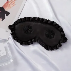 Máscara de dormir de seda negra con volantes y patrón floral bordado para buen descanso.